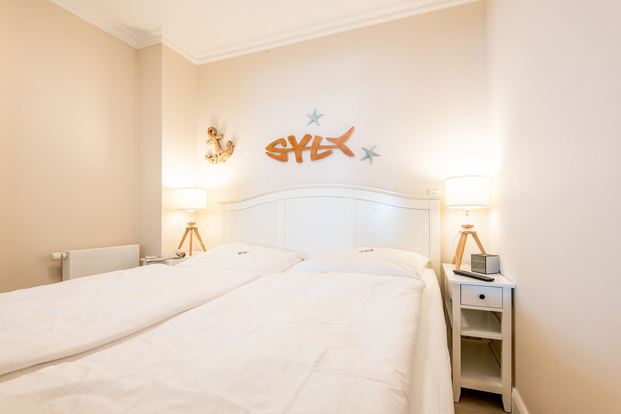 Camera d'albergo con due letti, una testiera bianca, lampade sui comodini e decorazioni a parete tra cui pesci e stelle.