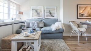 Una sala de estar moderna con un sofá gris, una mesita con un cuenco de vidrio y copas de vino, y una silla de mimbre.