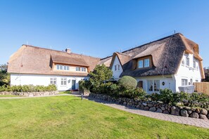 A large house with a thatched roof, a stone wall, and a well-maintained lawn.