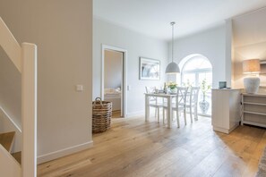 A modern kitchen with white cabinetry, a dining area with a white table and chairs, and a large window providing natural light.
