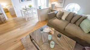 Ein modernes Wohnzimmer mit einem Holztisch, einem beigefarbenen Sofa mit Kissen und einem Essbereich mit einem weißen Tisch und Stühlen.