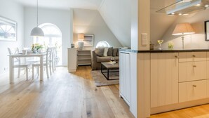 Eine moderne Küche mit weißen Schränken, ein Essbereich mit Tisch und Stühlen sowie eine gemütliche Sitzecke mit Sofa und Couchtisch.