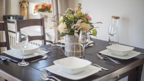 Une table à manger dressée avec de l’assiette, des bols et des couverts blancs, agrémentée d’un vase de fleurs et d’un verre d’eau.