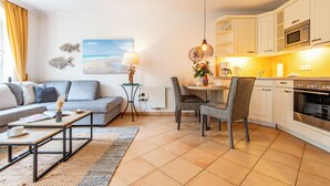 Ein modernes Wohnzimmer mit Sofa, Couchtisch und Essbereich. Es beinhaltet eine Küche mit weißen Schränken und Geräten.