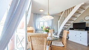 A dining area with wicker chairs, a glass table, and a white cabinet with a television. - Hell. Gemütlich. Zentral. Objekt-id: Has/28 (Westerland)