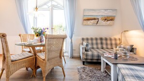 A cozy living room with a dining table, wicker chairs, a plaid sofa, and a painting of a beach scene. - Hell. Gemütlich. Zentral. Objekt-id: Has/28 (Westerland)
