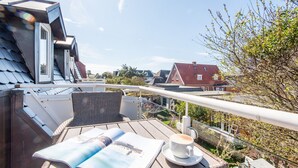 A balcony with a wicker chair, a table with a magazine and a cup of coffee, and a view of houses and trees. - Hell. Gemütlich. Zentral. Objekt-id: Has/28 (Westerland)