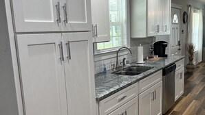Uma cozinha moderna com armários brancos, bancada de granito e piso de madeira.