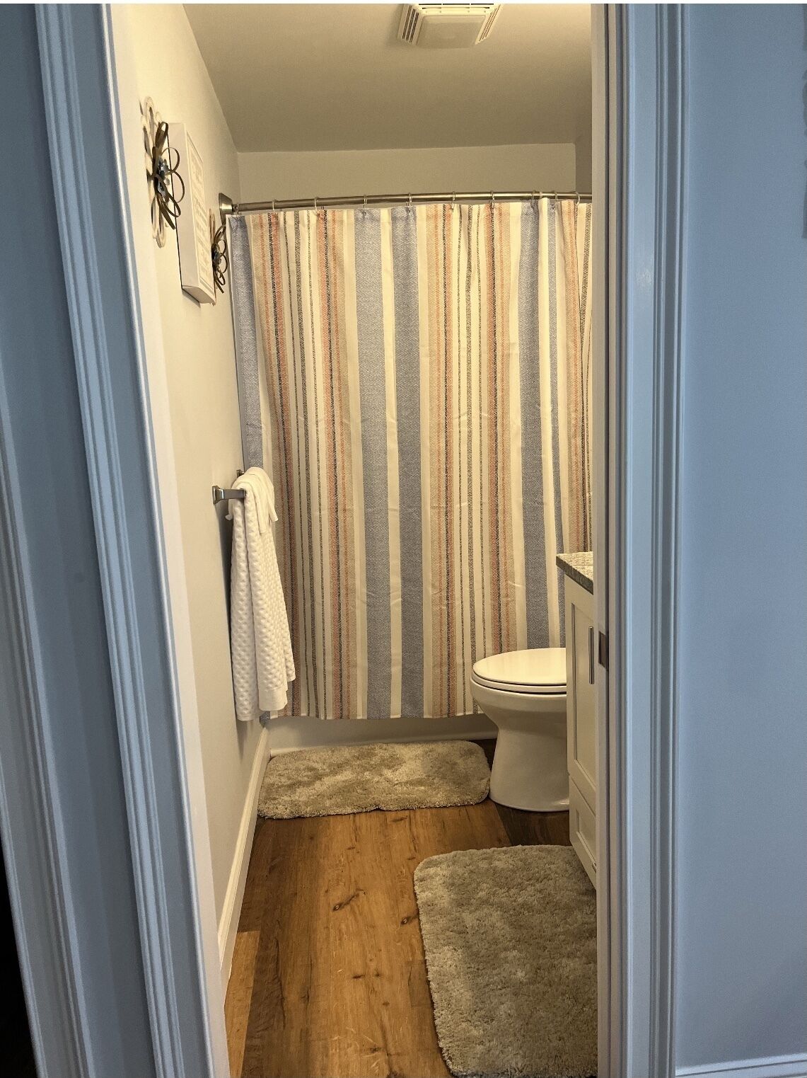 Een kleine badkamer met een gestreept douchegordijn, een toilet en een houten vloer.