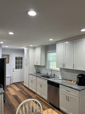 A modern kitchen with white cabinets, a stainless steel dishwasher, and a granite countertop.