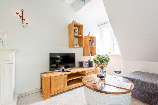A modern living room with a wooden entertainment unit, a flat-screen TV, and a round coffee table with a wine glass.