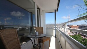 Ein Balkon mit Korbmöbeln, einem Tisch und freiem Blick auf die Stadtlandschaft und einen Turm.