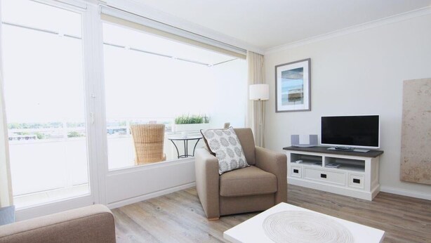 Ein modernes Wohnzimmer mit einer Couch, einem Couchtisch, einem Fernseher und einer Schiebeglastür, die auf einen Balkon führt.