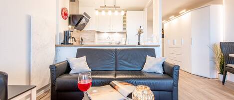 Una sala de estar moderna con un sofá de cuero negro, una mesa de centro con una revista, una copa de vino tinto y un jarrón decorativo.