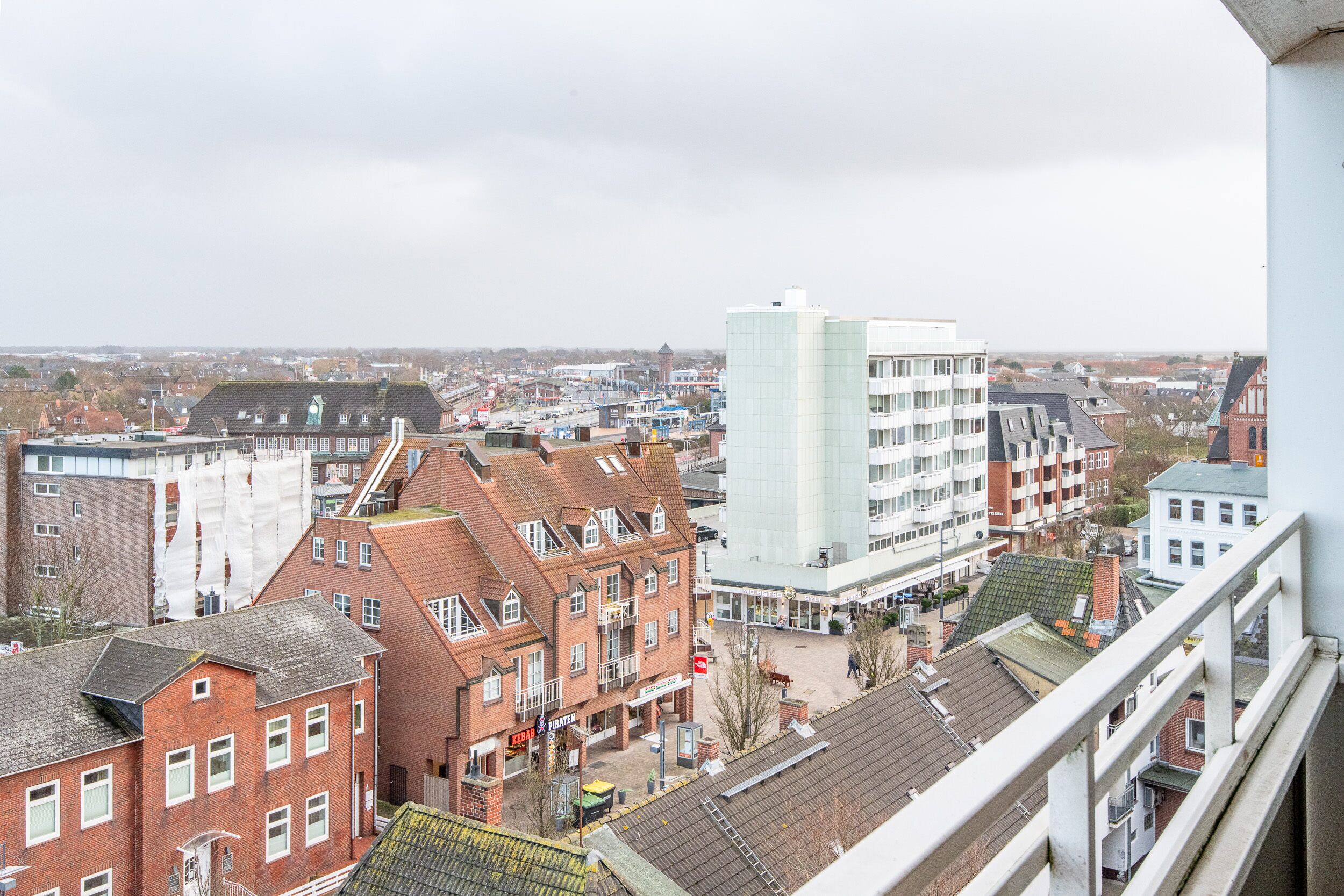 Un paysage urbain mêlant bâtiments traditionnels et modernes, notamment un imposant bâtiment blanc doté d’un toit plat et un bâtiment en briques rouges avec un toit en pente.