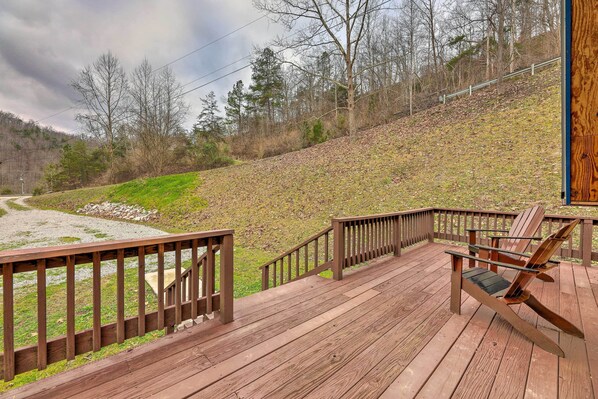 A wooden deck with a railing, a chair, and a view of a hillside with trees.