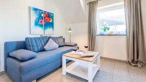 Un saló modern amb un sofà blau, una taula petita blanca i una finestra amb cortines.