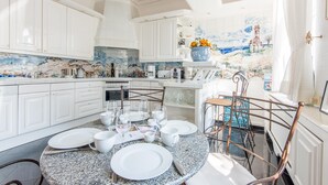Una cocina luminosa con armarios blancos, encimera de granito y comedor preparado para seis personas, con una mesa redonda y sillas metálicas.