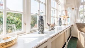Una habitación luminosa con ventanas amplias, un radiador y una silla de mimbre.
