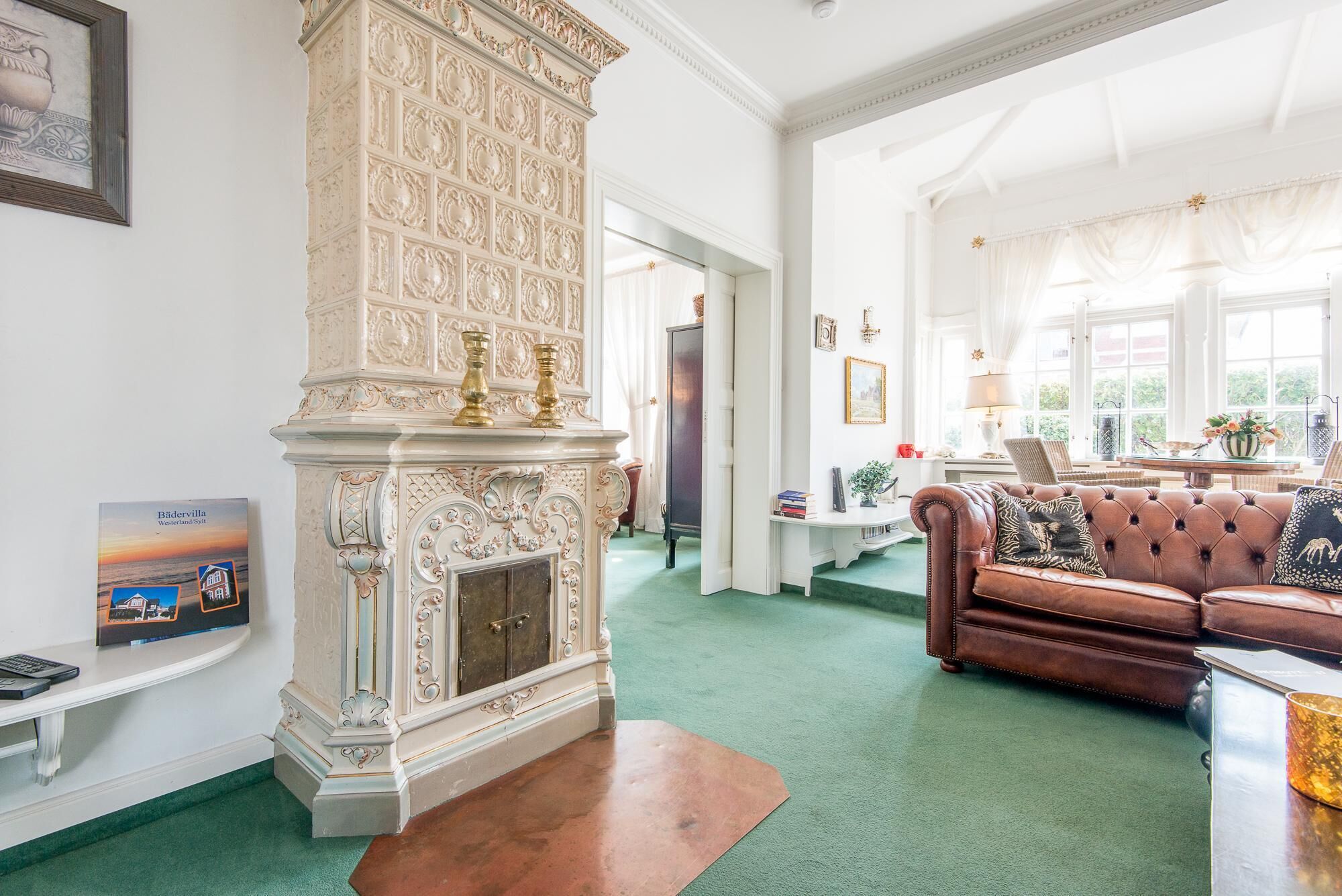 A spacious living room with a fireplace, a leather sofa, and a green carpet.