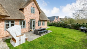A brick house with a thatched roof, a patio with a table and chairs, and a well-maintained lawn. - Dansk Hus Sylt List (List)