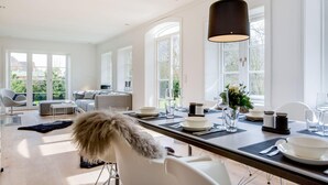 A bright, spacious dining area with a long table set for a meal, large windows, and a modern interior design. - Dansk Hus Sylt List (List)