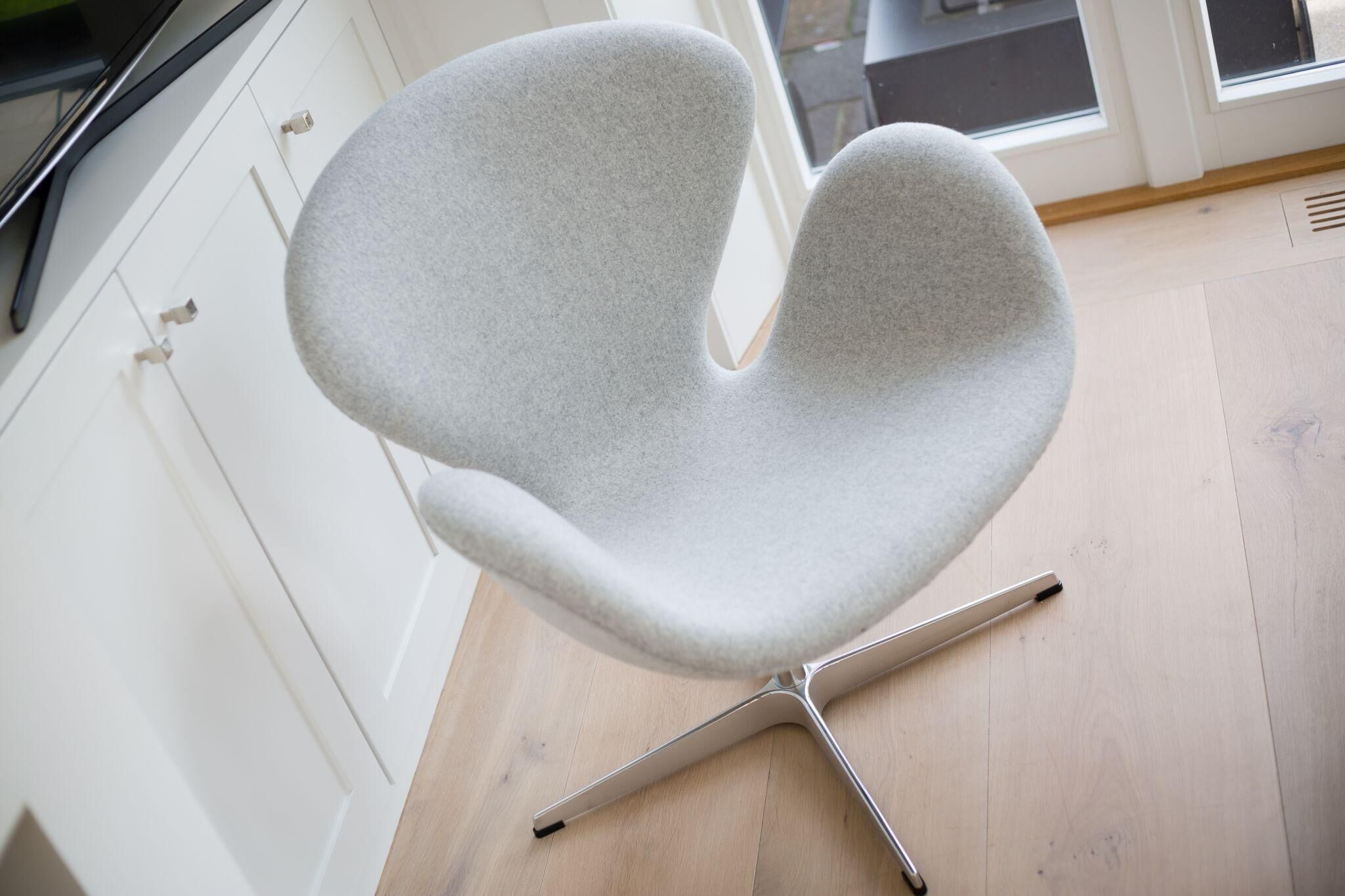 A modern chair with a unique design, placed in a room with white cabinets and a wooden floor.