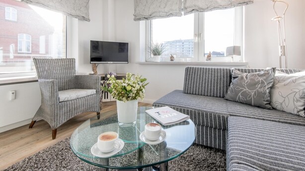 Ein modernes Wohnzimmer mit Sofa, Sessel, Glastisch und einem Blumentopf.
