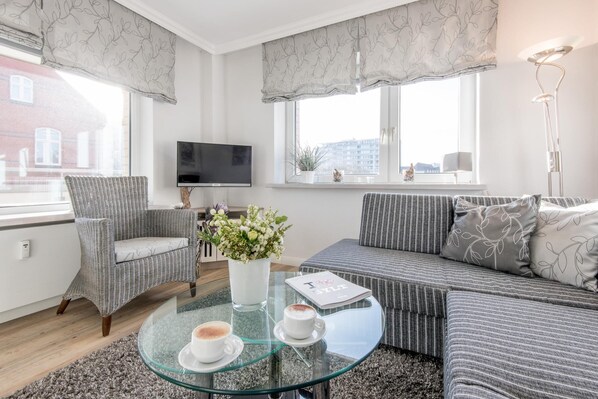 A modern living room with a sofa, armchair, glass coffee table, and a potted plant.