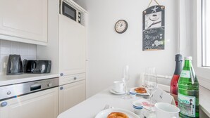 Eine saubere, moderne Küche mit weißen Schränken, einem Siemens-Ofen, einer Mikrowelle und einer Frühstücksecke mit einem Croissant, Kaffeetassen und einer Flasche Apetite.