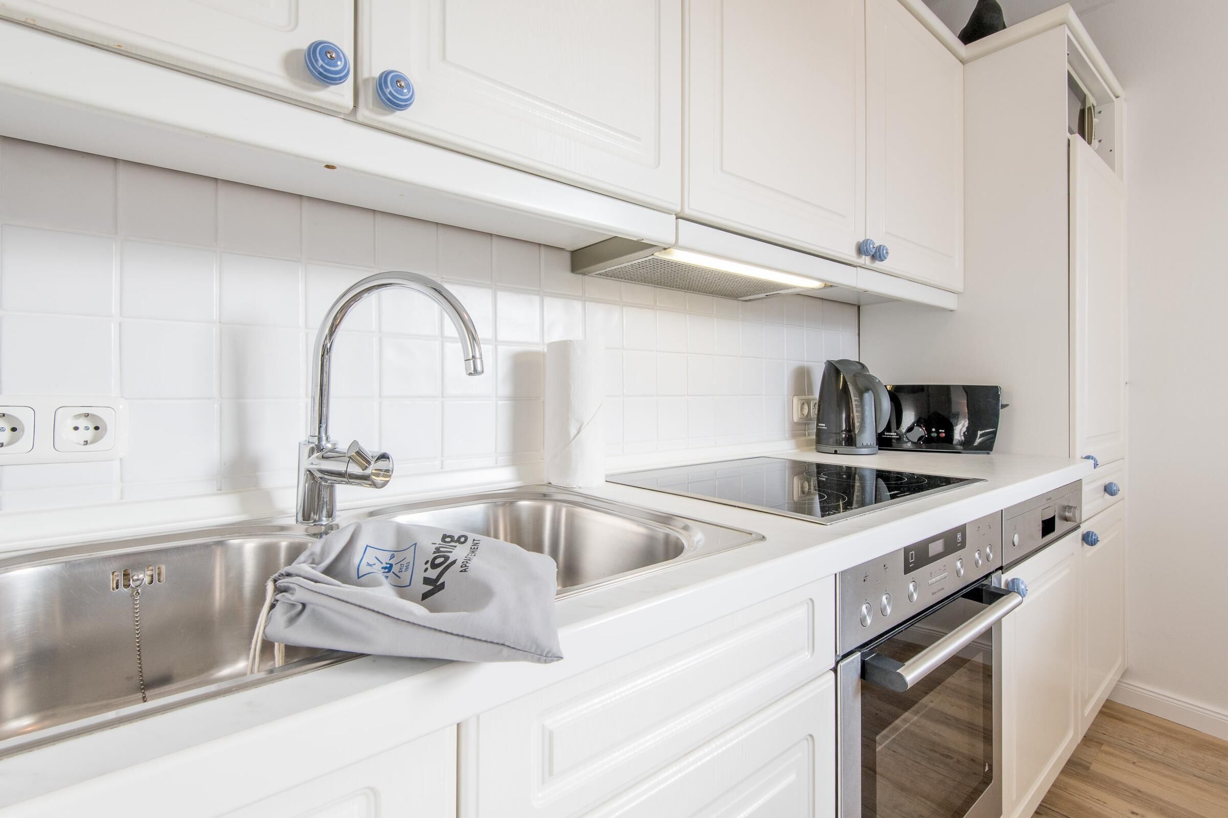 A modern kitchen with white cabinetry, stainless steel appliances, and a built-in oven.