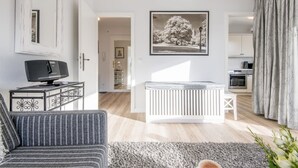 Ein modernes Wohnzimmer mit einer Couch, einem Fernseher auf einem Schrank, einer Heizung und einem gerahmten Bild an der Wand.