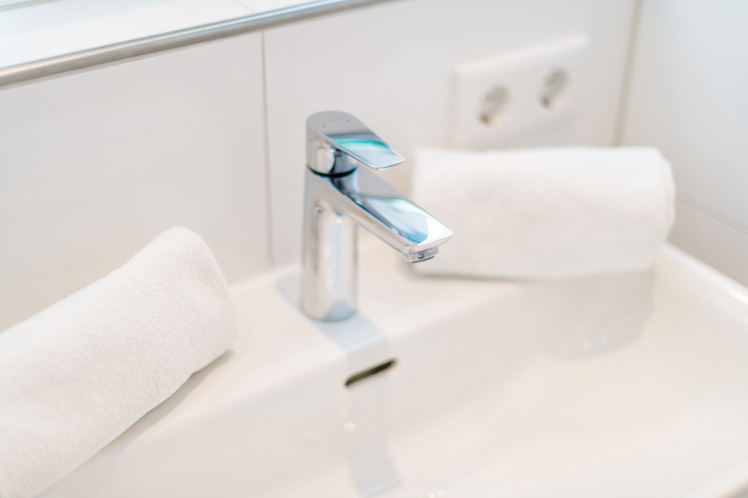 A modern bathroom with a chrome faucet, a white sink, and a towel.