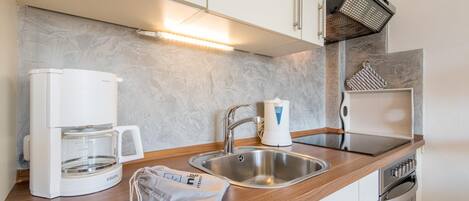 A modern kitchen with a coffee maker, kettle, sink, and oven.