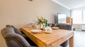 Een eetruimte met een houten tafel gedekt voor twee personen, een vaas met bloemen en een televisie op de achtergrond.