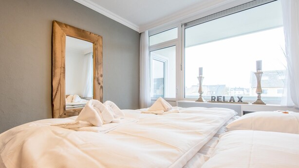 Een hotelkamer met twee bedden, een grote spiegel en een raam met uitzicht op gebouwen.