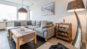 Een moderne woonkamer met een grijze bank, een houten salontafel en een wijnrek.
