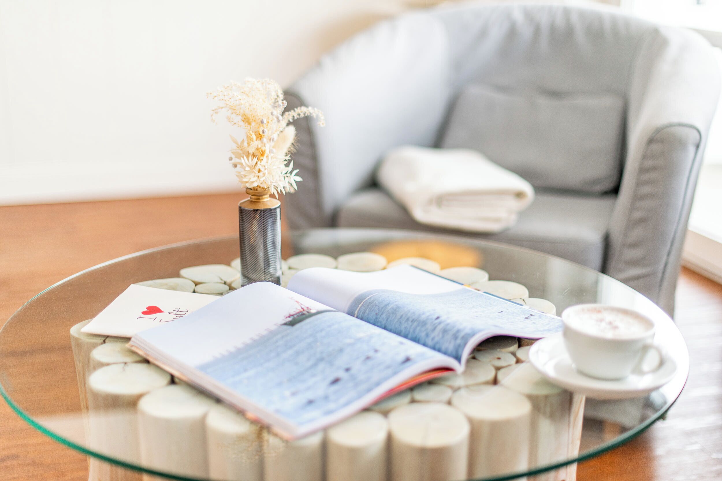 A glass table with a book, a cup of coffee, and a decorative vase.