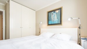 A neatly made bed with white linens, a framed painting above it, and a bedside lamp on the right. - Gemütlich. Zentral. Strandnah. Objekt-id: Hdb/24 (Westerland)