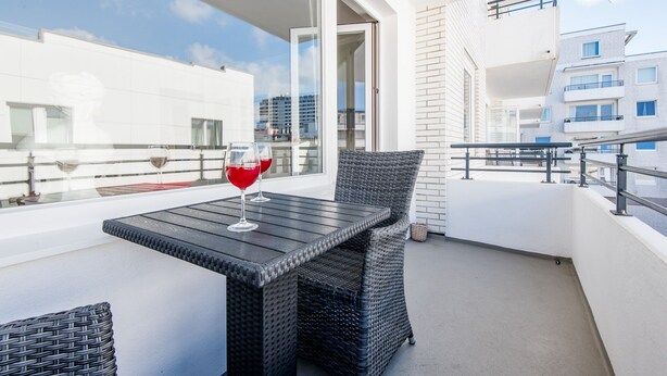 A balcony with a table and chairs, a glass of red wine, and a view of buildings. - Gemütlich. Zentral. Strandnah. Objekt-id: Hdb/24 (Westerland)