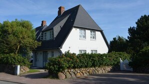 Une maison à deux étages, dotée d’un toit à forte pente, de murs extérieurs blancs et de fondations en pierre.