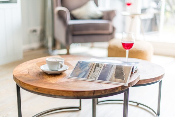 A round wooden table with a cup and saucer, a glass of red wine, and a magazine.
