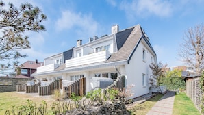 A two-story house with a stone retaining wall, a wooden fence, and a pathway leading to the front door. - Stylish. Terrasse. Strandnah. Objekt-id: Hf/03 (Westerland)