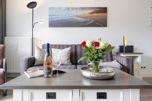 A room with a sofa, a table with a bottle, a glass, and a vase with flowers.
