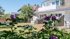 Ein Wohnhaus mit eingezäuntem Garten, einer Holzterrasse und einem Satteldach.