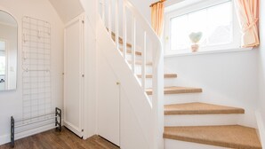 Eine Treppe mit weißen Geländern und Holzstufen, die zu einem Raum mit Fenster und einer kleinen Pflanze führt.