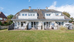 Ein zweigeschossiges Haus mit überdachter Terrasse, einem eingezäunten Garten und blauem Himmel.