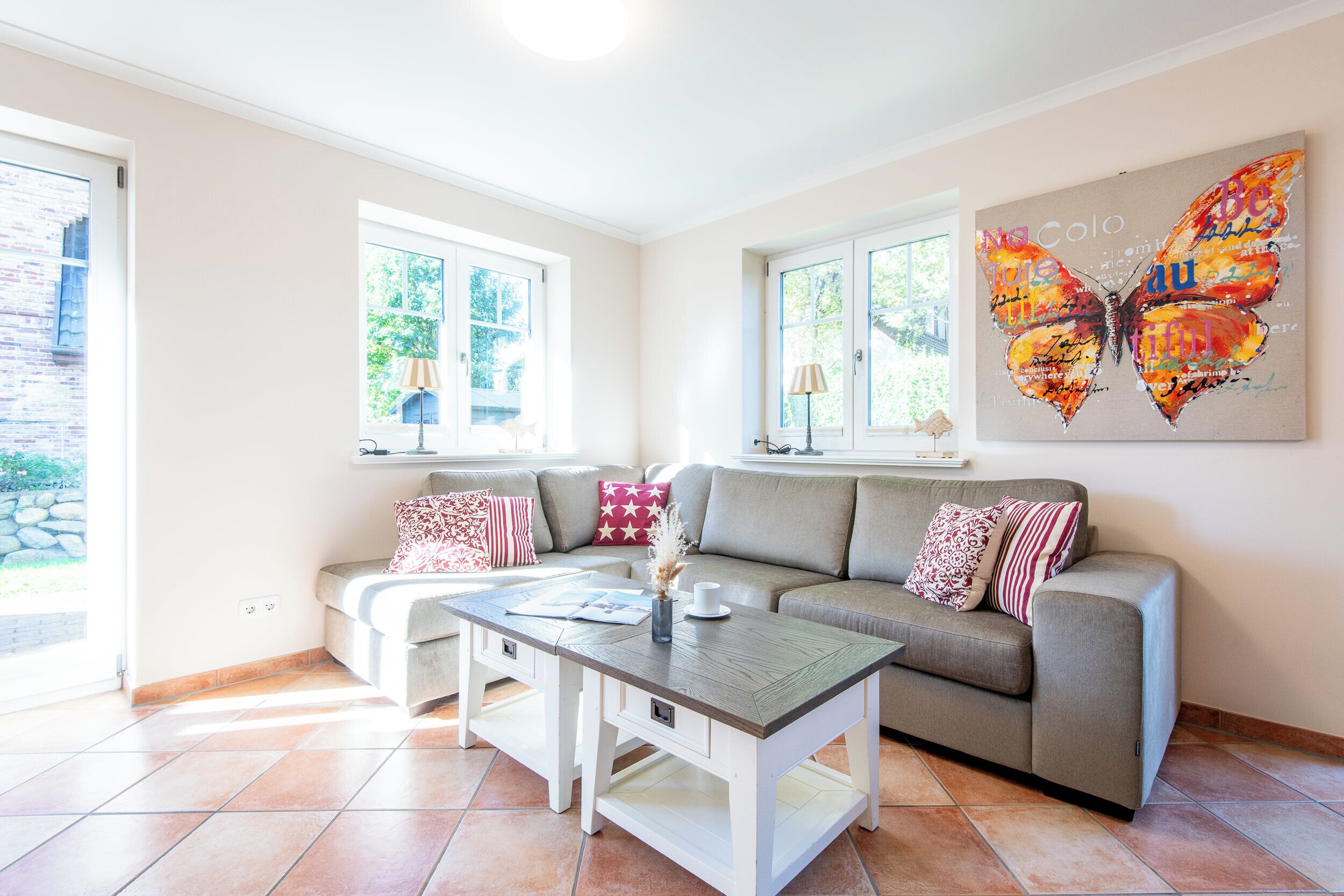 A living room with a grey sofa, a coffee table, and a large butterfly artwork on the wall.