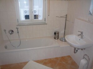 Une salle de bain avec une baignoire, une douche, un lavabo et une fenêtre avec un rideau.