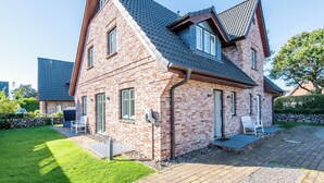 A two-story brick house with a sloped roof, a stone wall, and a paved patio with outdoor seating. - Exklusiv. Garten. Sauna. Objekt-id: Gkw/4b (Westerland)